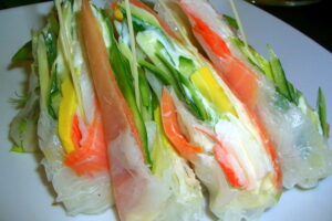 Поєднання копченого лосося, загорнутого в рисовий папір, з авокадо, огірком та крабовими паличками