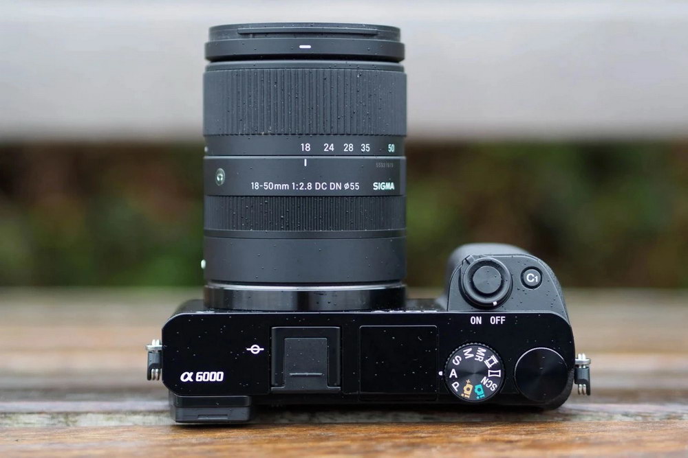 Об’єктив Sigma 18-50mm f/2.8 DC DN встановлений на камеру Sony Alpha на дерев’яному столі Об’єктив Sigma 18-50mm f/2.8 DC DN встановлений на камеру Sony Alpha на дерев’яному столі
